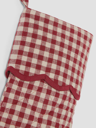 A close-up of a red and cream gingham quilted fabric stocking with a scalloped red trim and a hanging loop, shown against a light gray background.