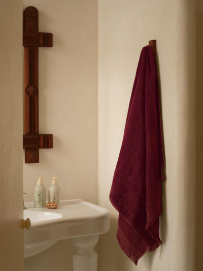 Bathroom with a sink, toiletries, and a maroon towel hanging on a wooden rack.