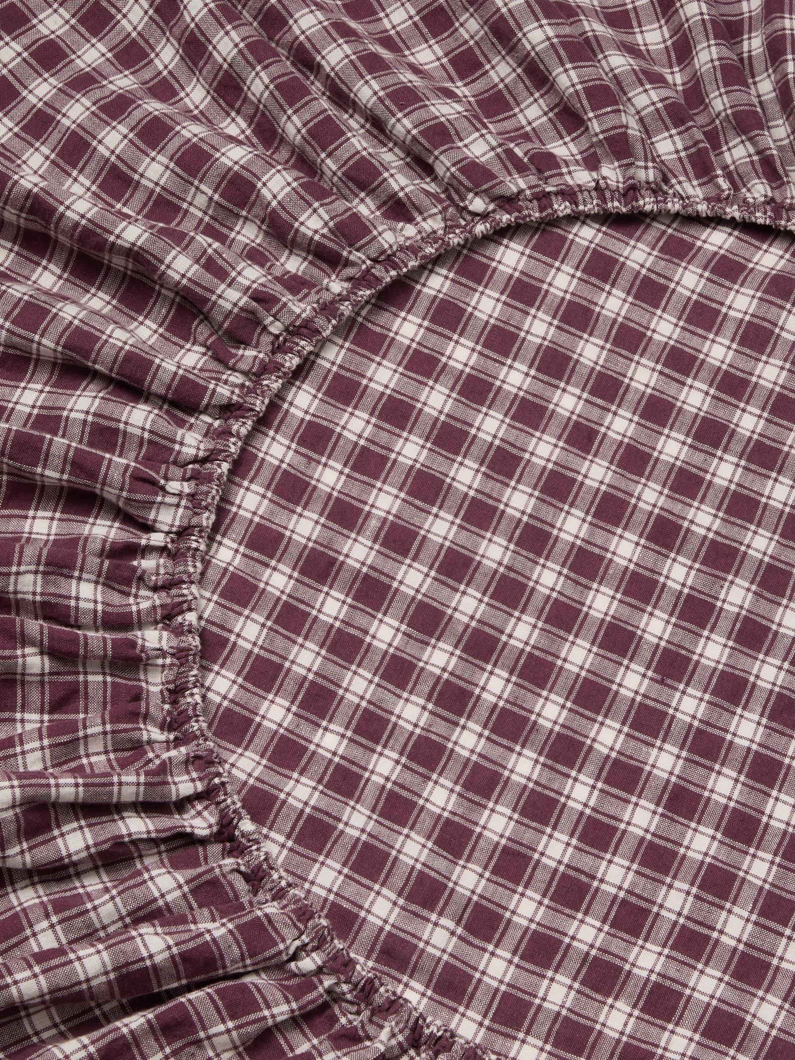 Close-up of a plaid fabric with a gathered elasticized edge, showing a burgundy and white checkered pattern.