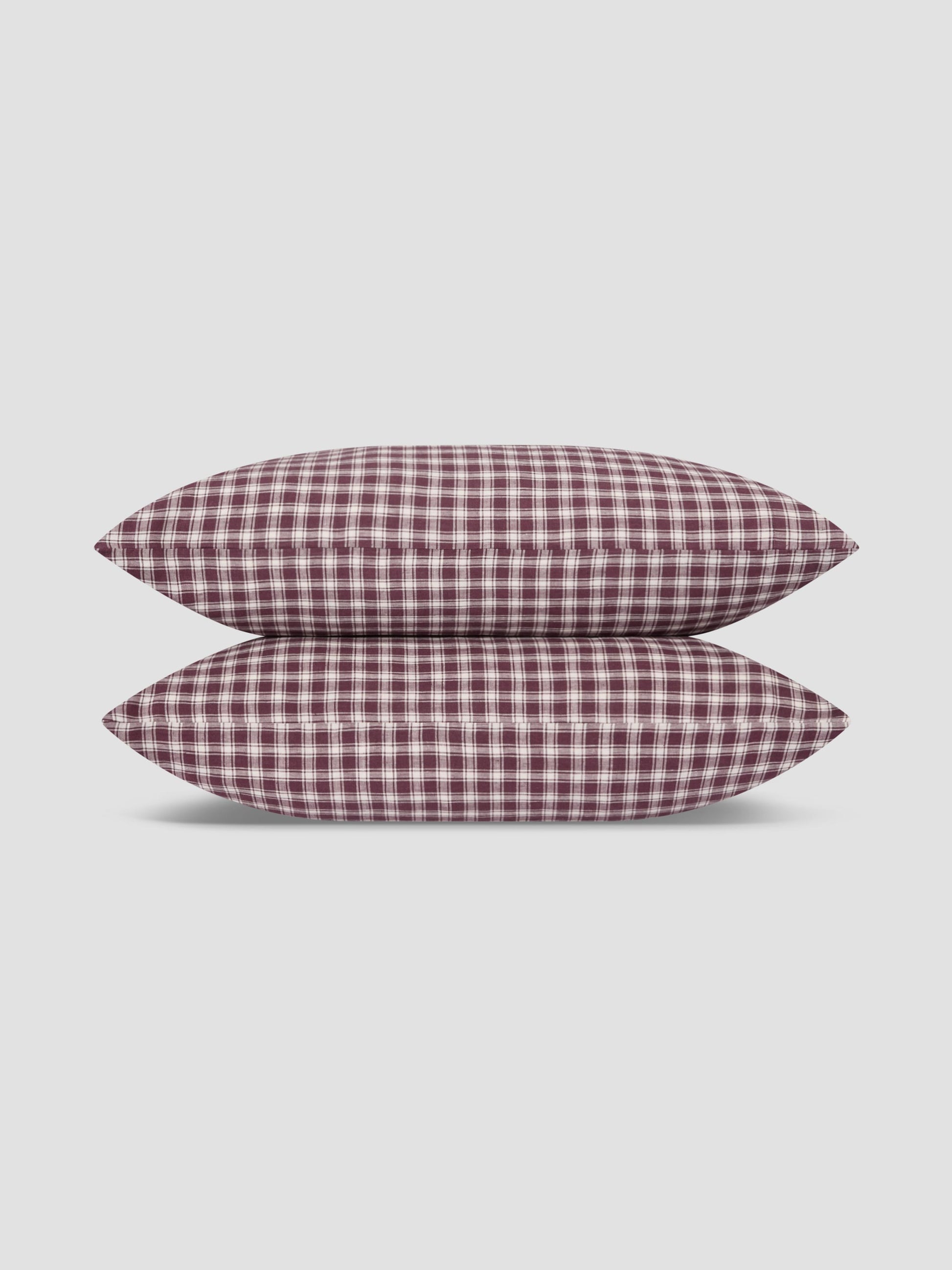 Two pillows stacked vertically, featuring a classic red and white gingham checkered pattern, set against a solid light gray background.