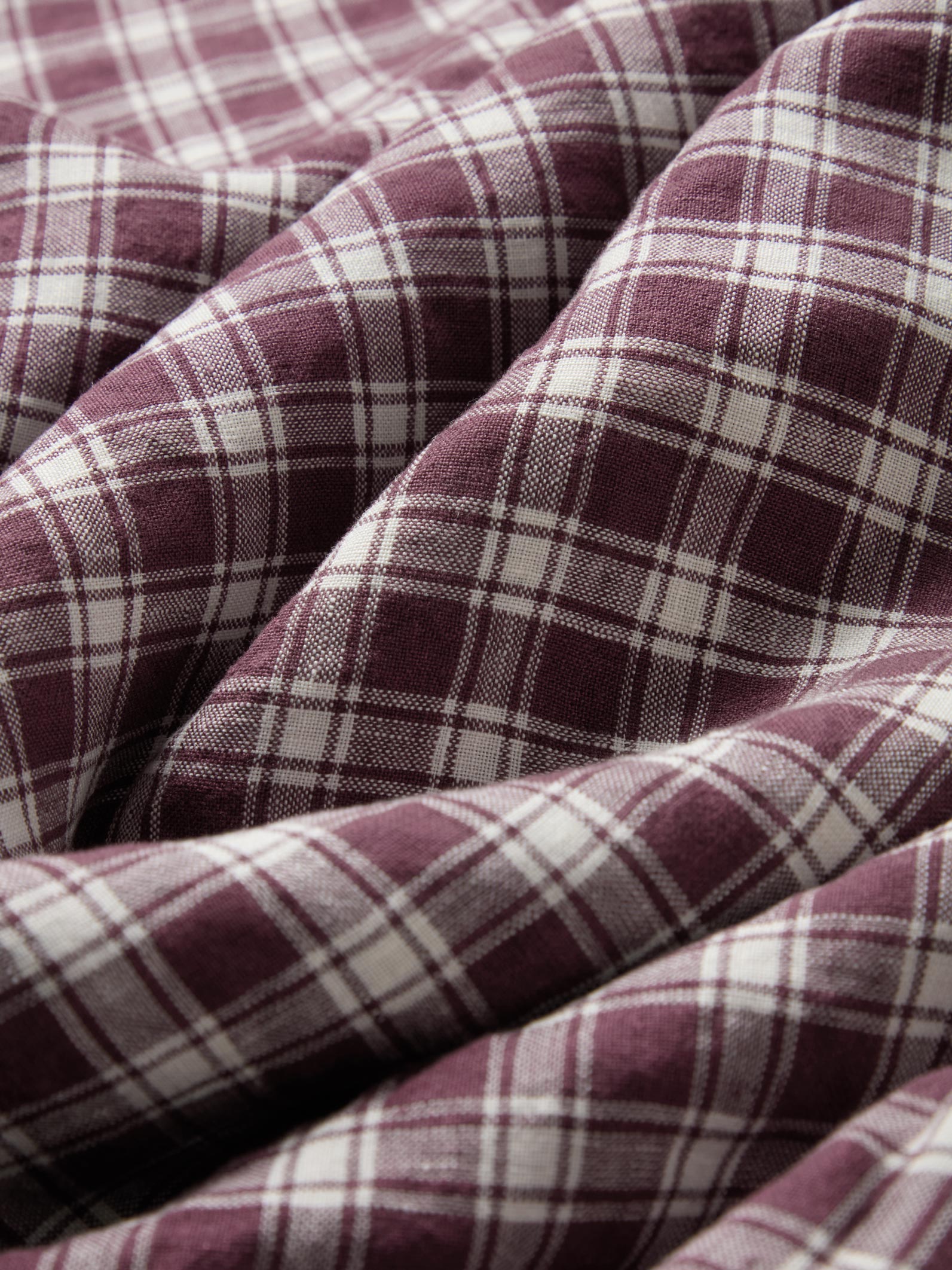 A close-up of draped plaid fabric in a dusty burgundy and off-white tartan pattern.