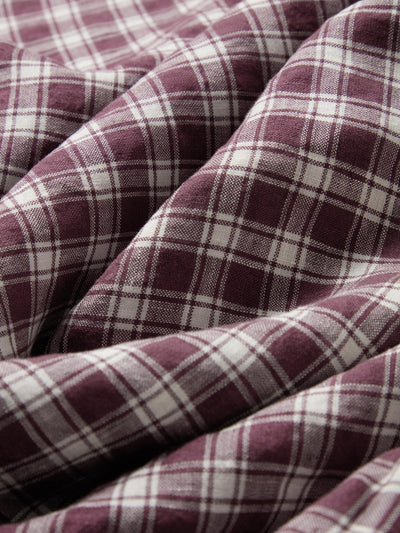 A close-up of draped plaid fabric in a dusty burgundy and off-white tartan pattern.