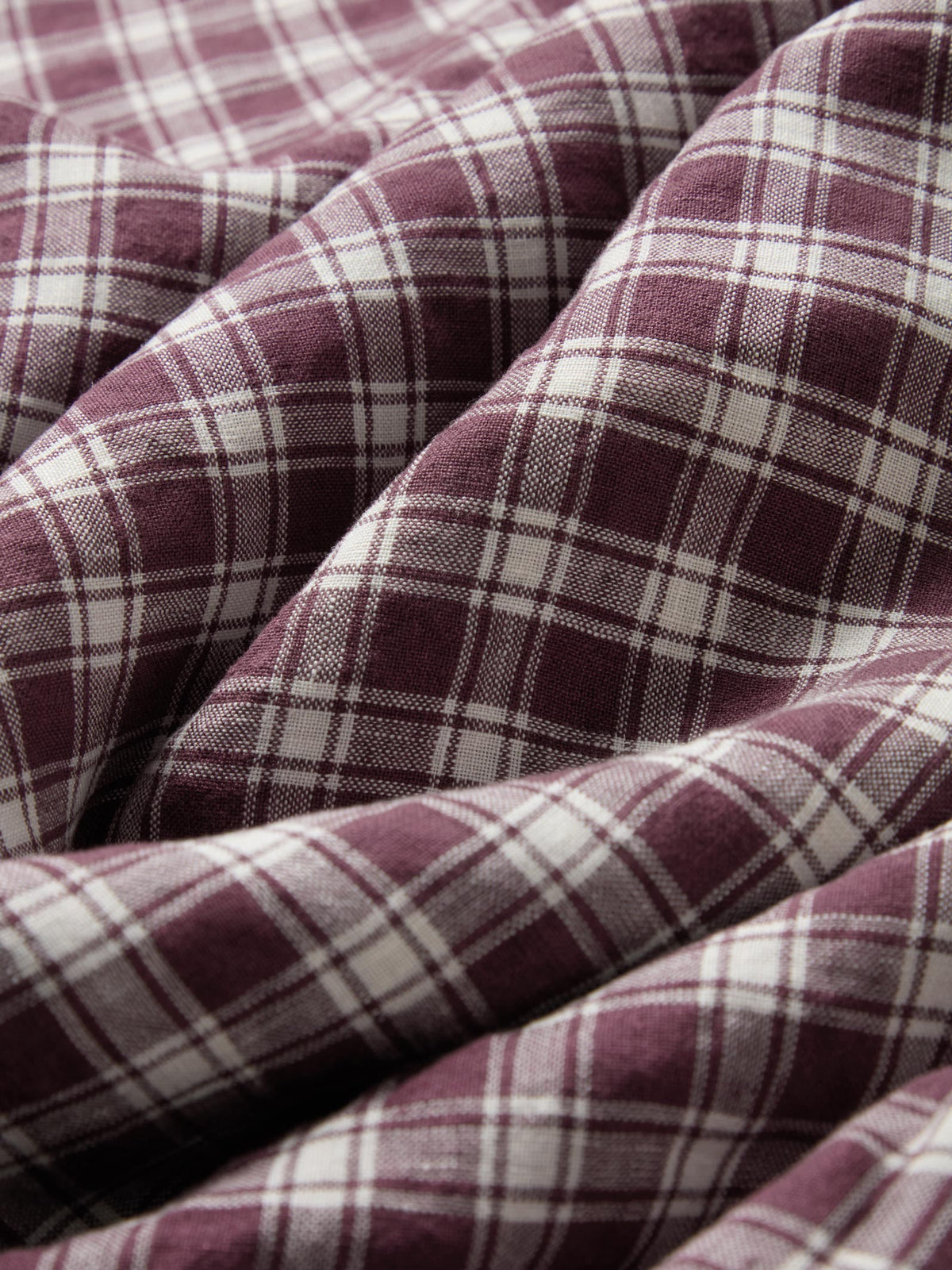 A close-up of draped plaid fabric in a dusty burgundy and off-white tartan pattern.