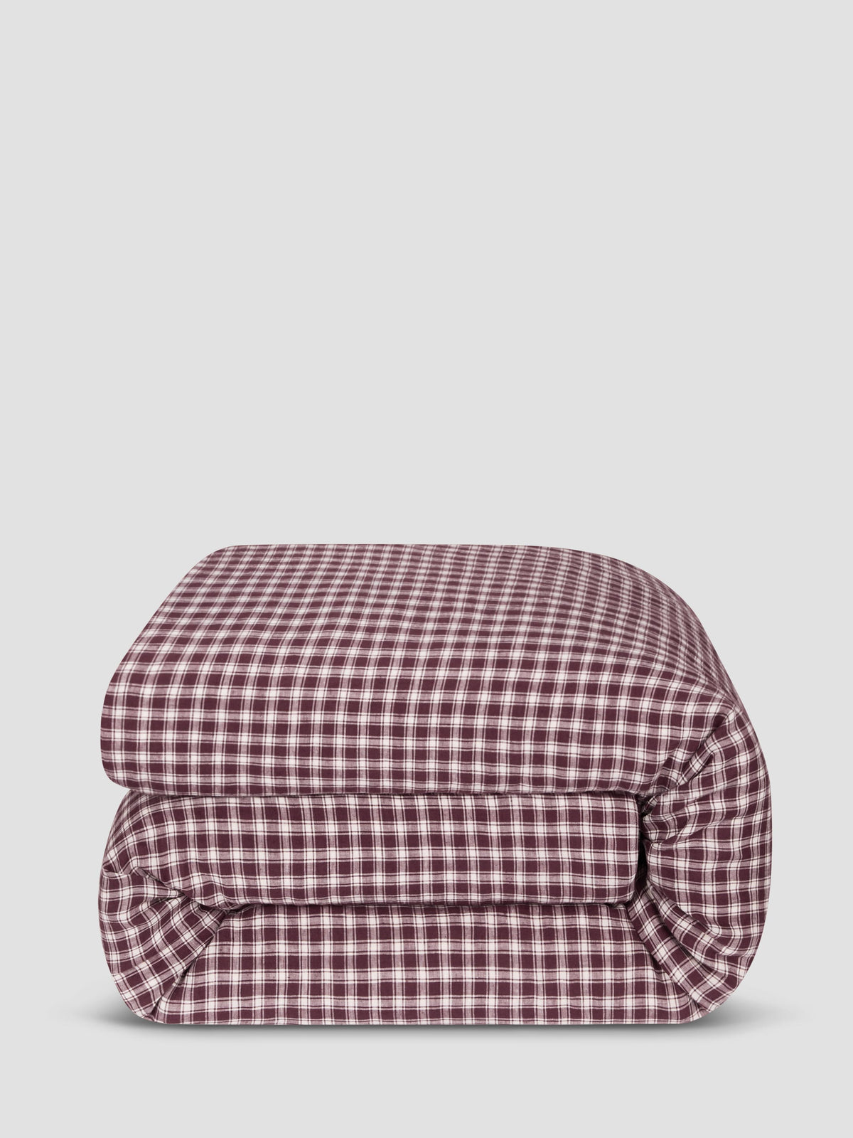 A folded checkered comforter in a burgundy and white gingham pattern, photographed against a solid light gray background.