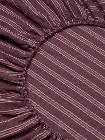 Close-up of a striped fabric with a gathered elastic edge, showing a dusty purple base with thin pink and white diagonal stripes.