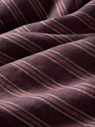 A close-up of draped fabric with a deep plum-purple base and diagonal stripes in muted pink and light beige.