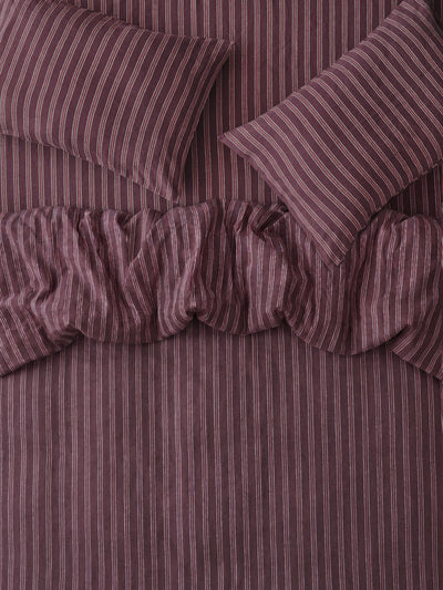 A close-up of a striped bedding set in a muted plum-purple color, featuring a ruffled duvet cover and two matching pillowcases.