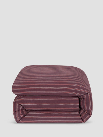 A folded duvet cover or comforter, featuring a dark burgundy base with thin, evenly spaced light pink stripes, set against a solid light gray background.