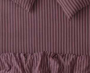 A close-up of a striped bedding set in a muted plum purple color, featuring a ruffled duvet cover and two matching pillows with vertical stripes.