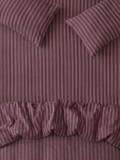 A close-up of a striped bedding set in a muted plum purple color, featuring a ruffled duvet cover and two matching pillows with vertical stripes.