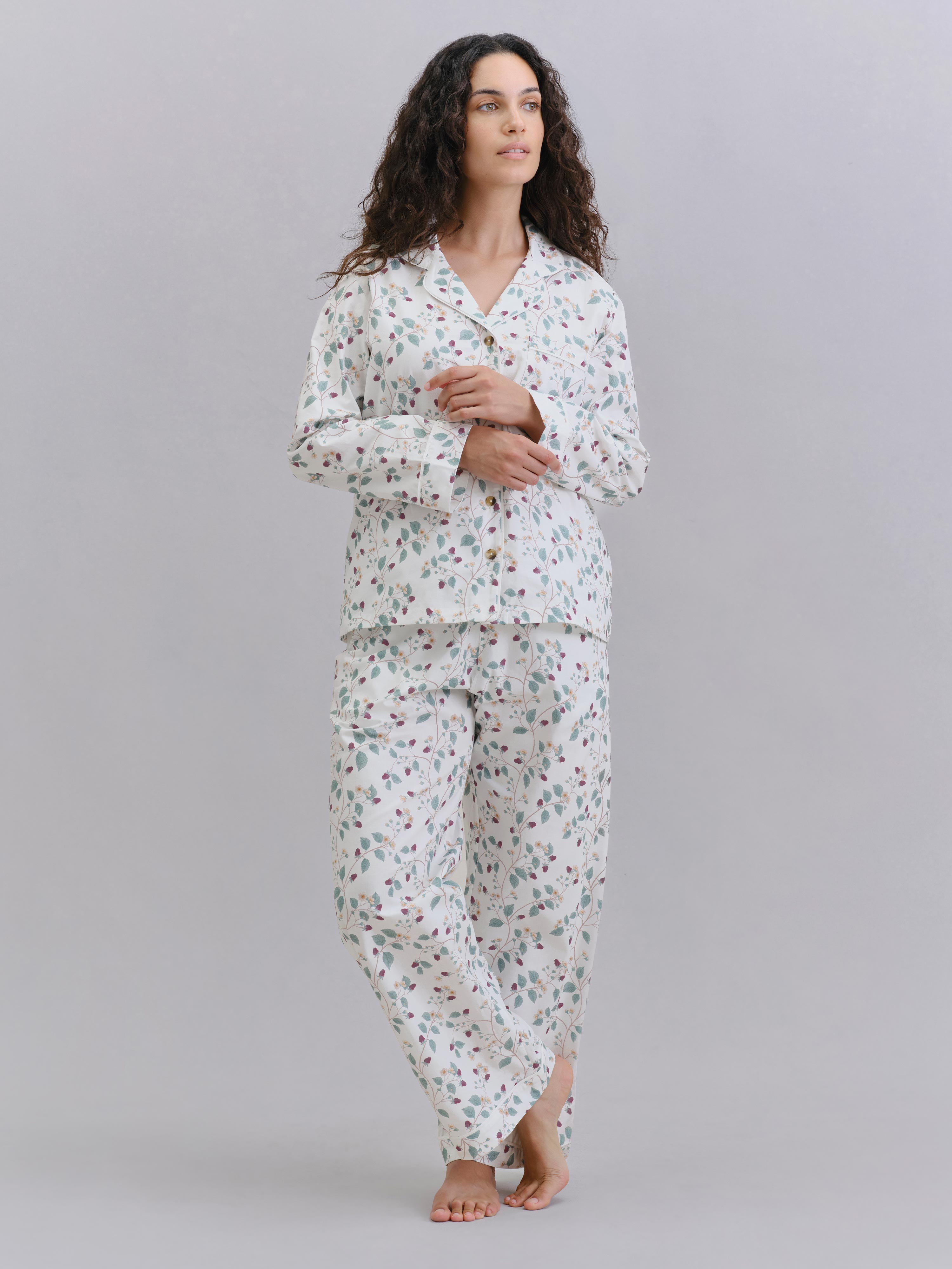A woman modeling a two-piece pajama set with a white base and a small multicolor floral print, standing against a solid light gray studio background.