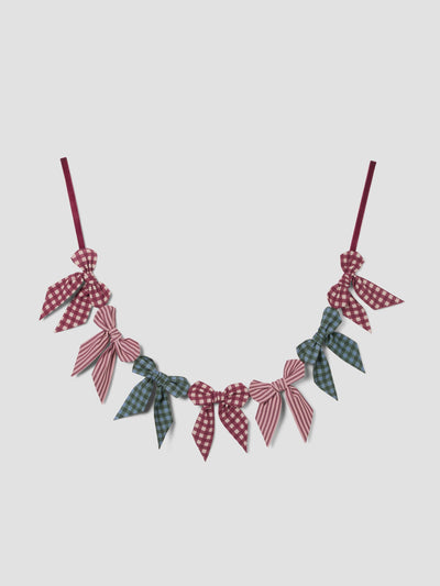 A decorative garland of fabric bows in red, pink, and green plaid and checkered patterns, suspended against a light gray background.
