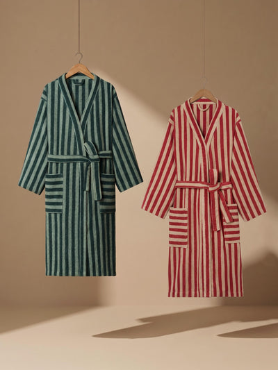 Two striped bathrobes hanging on wooden hangers against a warm beige wall. The robe on the left is dark green with vertical stripes, and the robe on the right is red with vertical stripes.