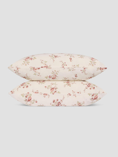 Two pillows stacked vertically, featuring a delicate pink and green floral pattern on a warm cream background, set against a solid light gray studio backdrop.