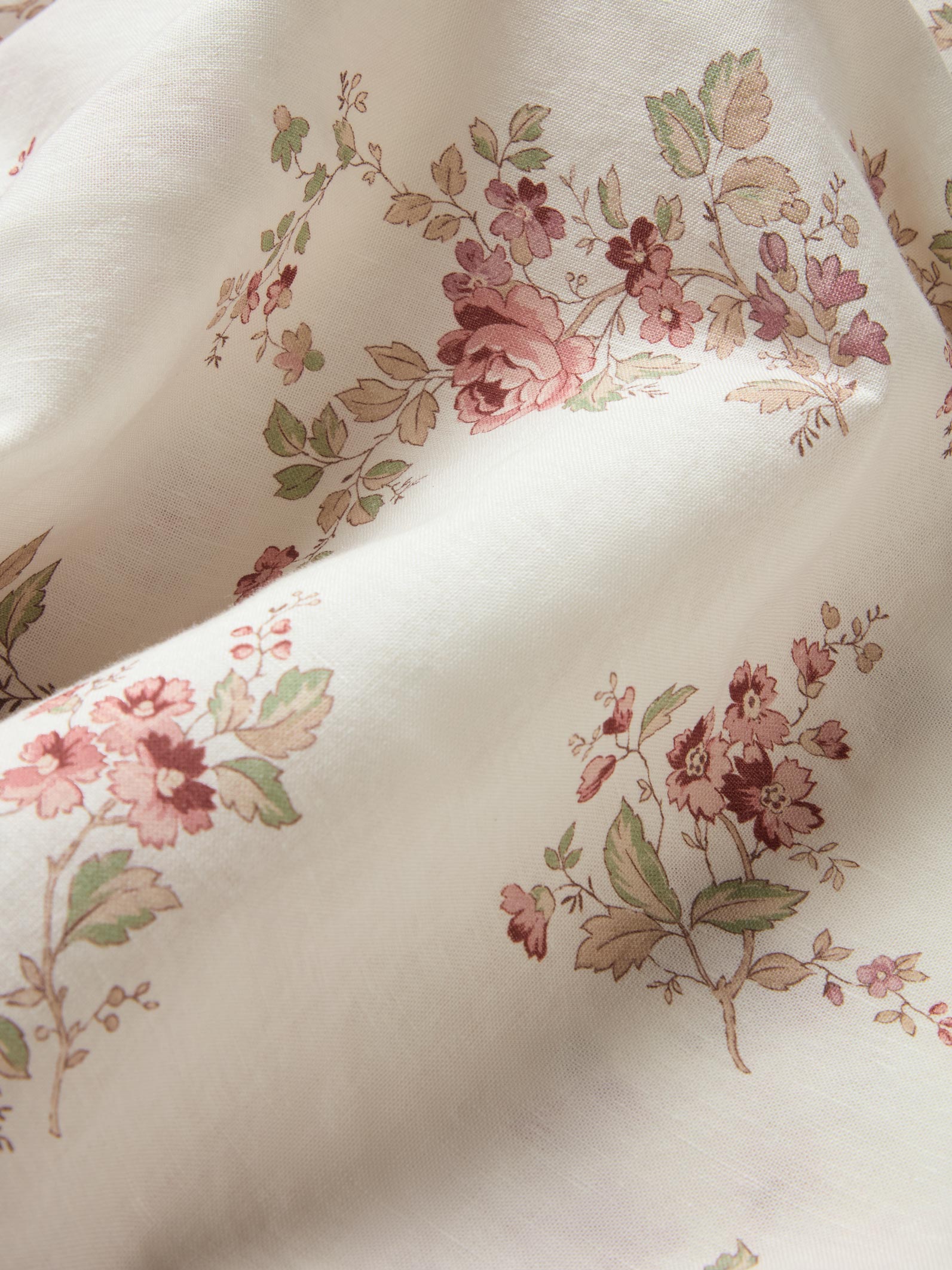 A close-up of a cream-colored fabric with a delicate, vintage-style floral print in dusty pink, mauve, and muted green.