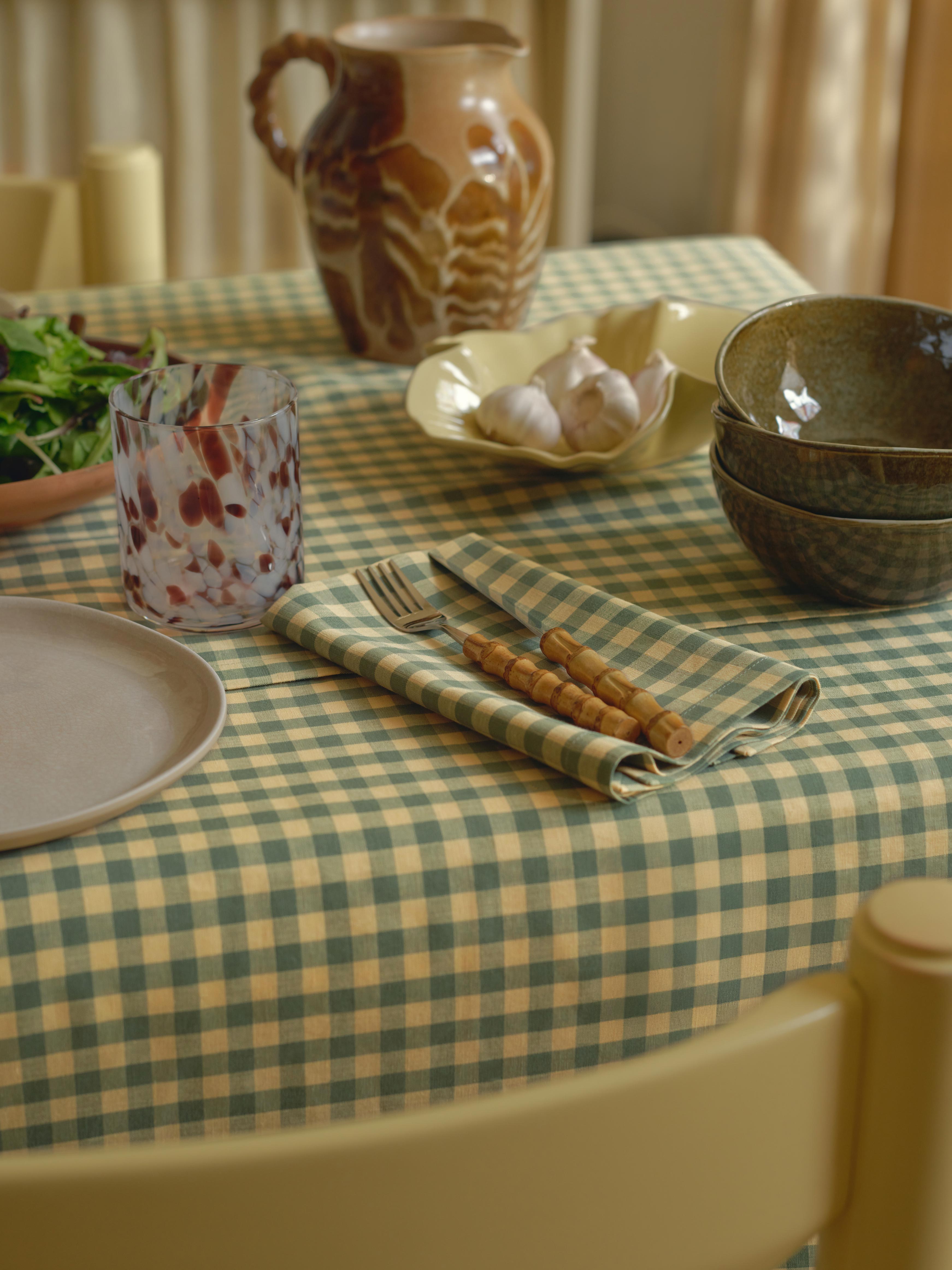 Dining table setting with checkered tablecloth, ceramicware, and cutlery.