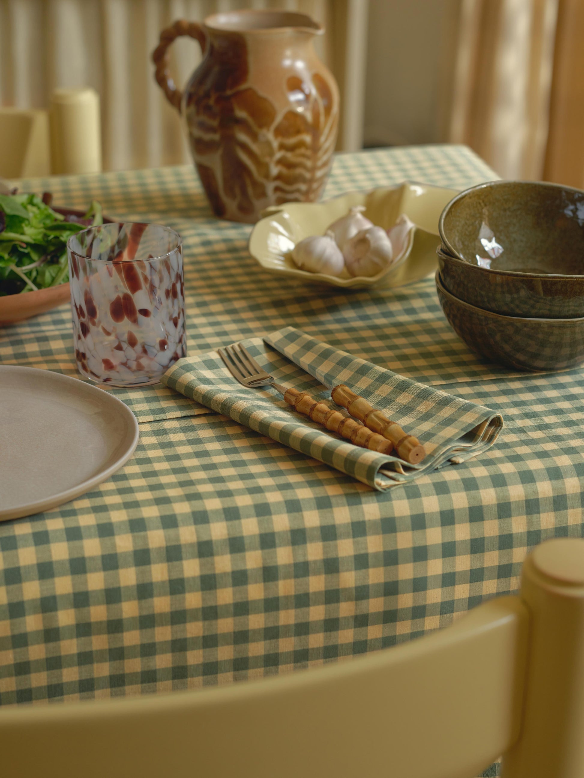 Dining table setting with checkered tablecloth, ceramicware, and cutlery.