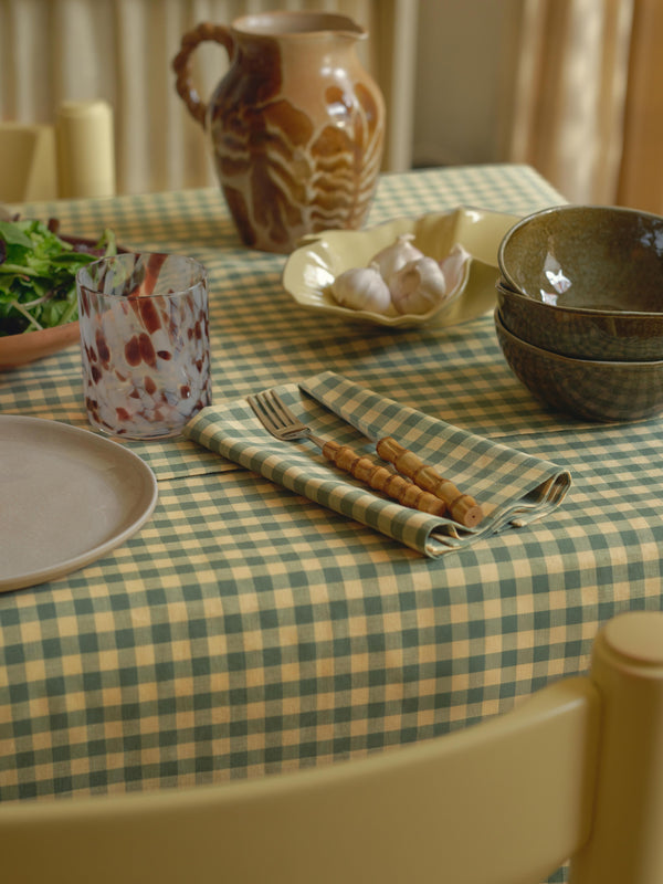 Dining table setting with checkered tablecloth, ceramicware, and cutlery.