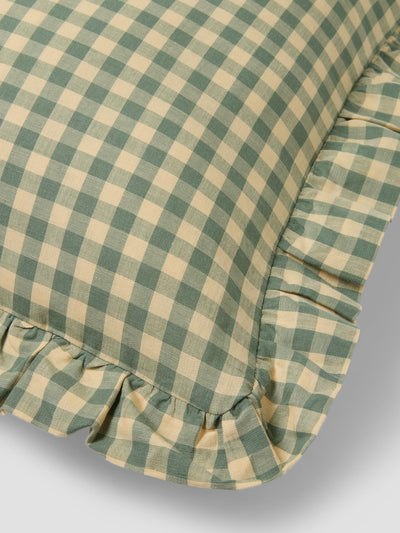 Green and beige checkered pillow with ruffled edge on a light gray background