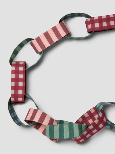 A circular woven chain of patterned fabric loops in pink, green, and red gingham, arranged on a light gray background.