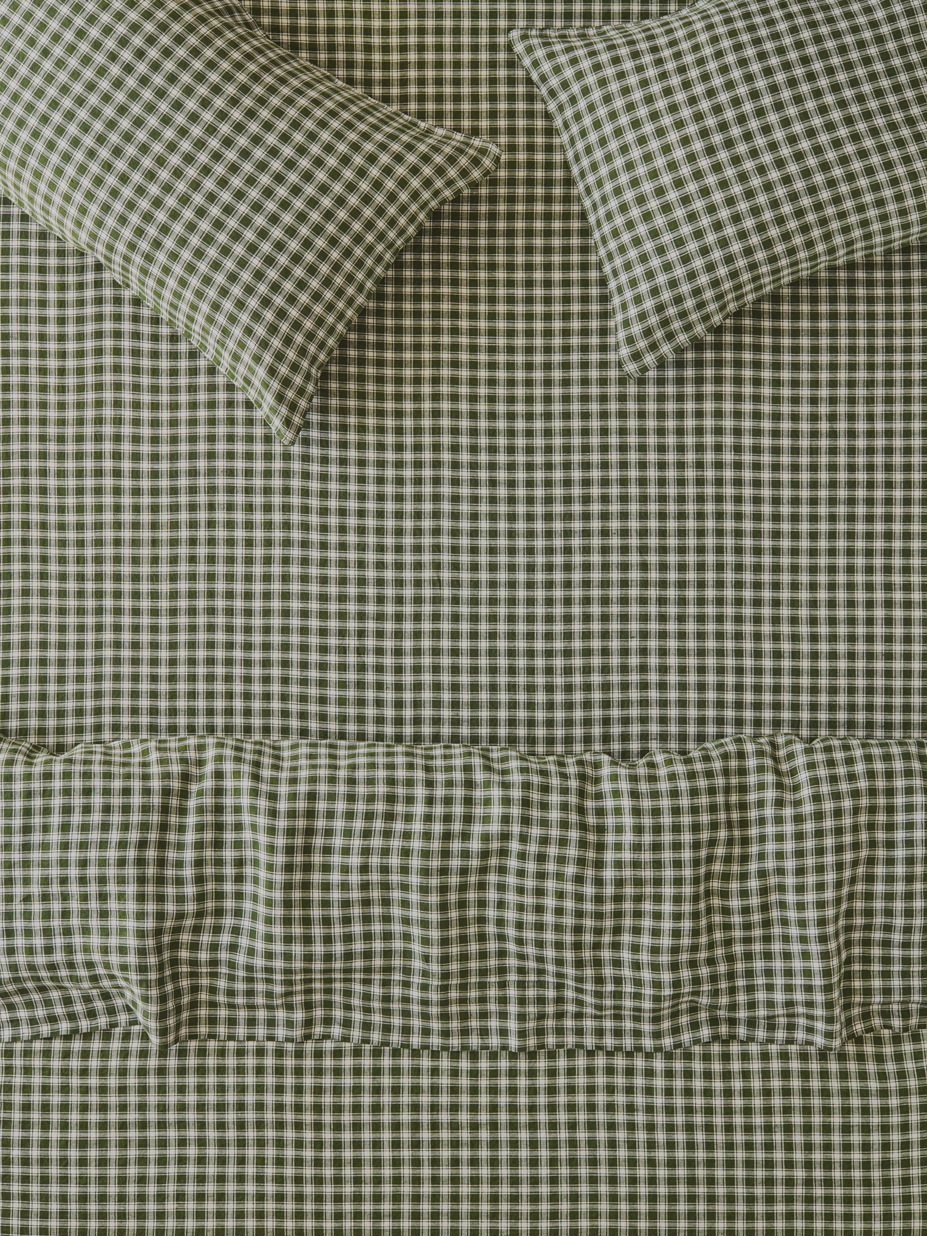 A close-up of a bed dressed in matching gingham bedding, featuring a sheet, pillowcases, and a ruffled duvet cover in a fern green and white check pattern.