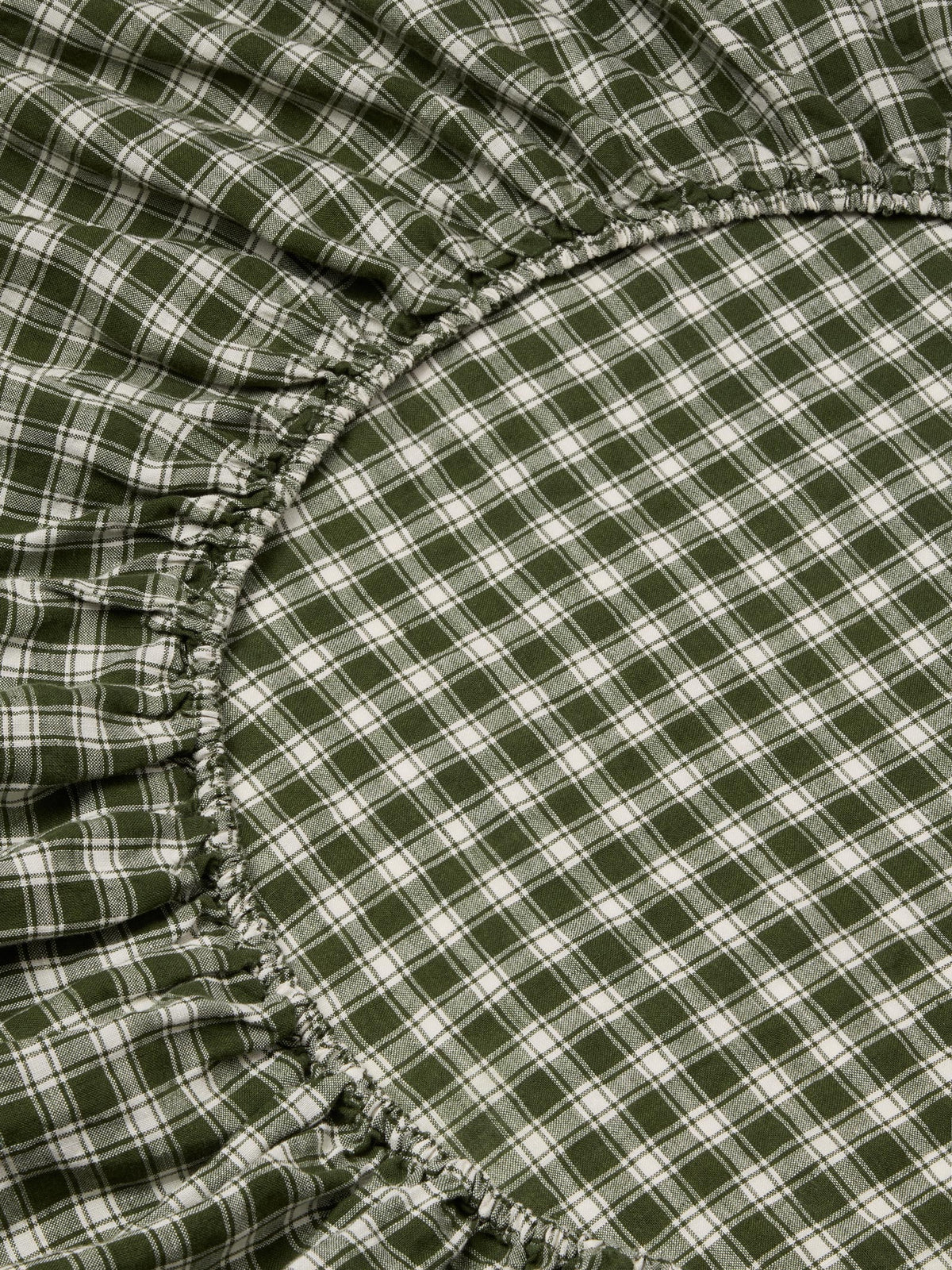 Close-up of a green and white plaid fabric with gathered elasticized edges, likely a fitted sheet or bedding component.