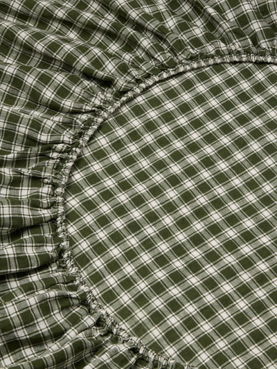 Close-up of a green and white plaid fabric with gathered elasticized edges, likely a fitted sheet or bedding component.