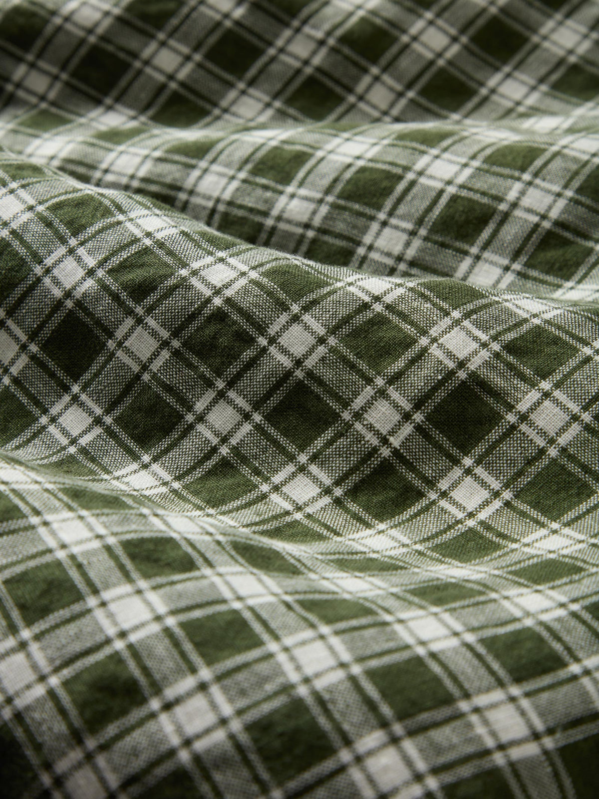 A close-up of a green and white plaid fabric with a soft, draped texture.