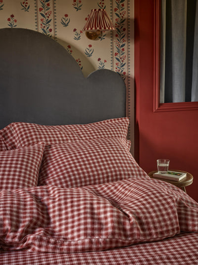Red and white gingham check bedding set with matching pillows and duvet, styled on a bed with a dark gray cloud-shaped headboard in a bedroom with red walls and floral wallpaper.