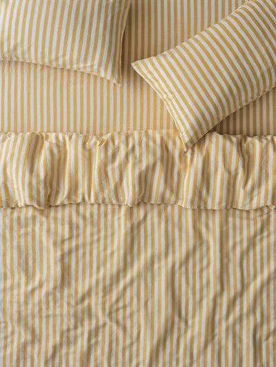 Yellow and white striped bedding set including a duvet cover with a ruffled hem and two matching pillowcases.