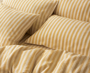 Yellow and cream striped bedding set with matching pillowcases on a bed, featuring a matching patterned wallpaper background.