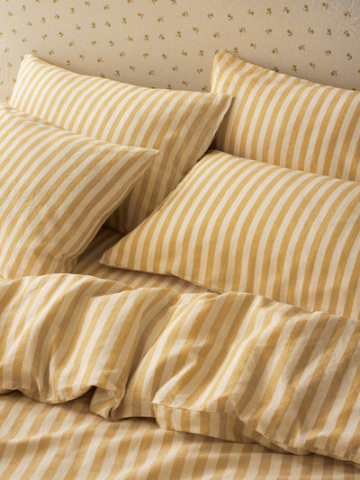Yellow and cream striped bedding set with matching pillowcases on a bed, featuring a matching patterned wallpaper background.