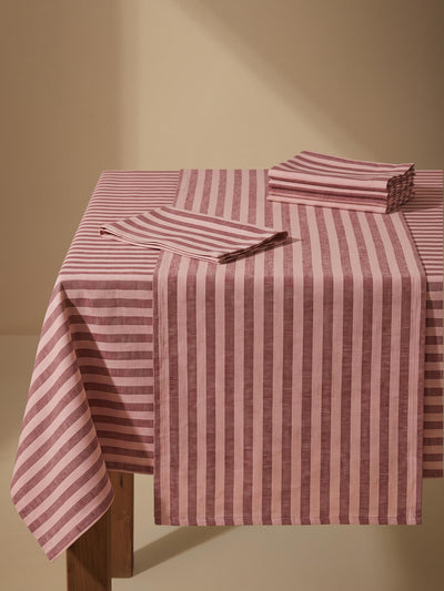 A pink and red striped tablecloth draped over a wooden table, with matching folded napkins on top, set against a warm beige background.