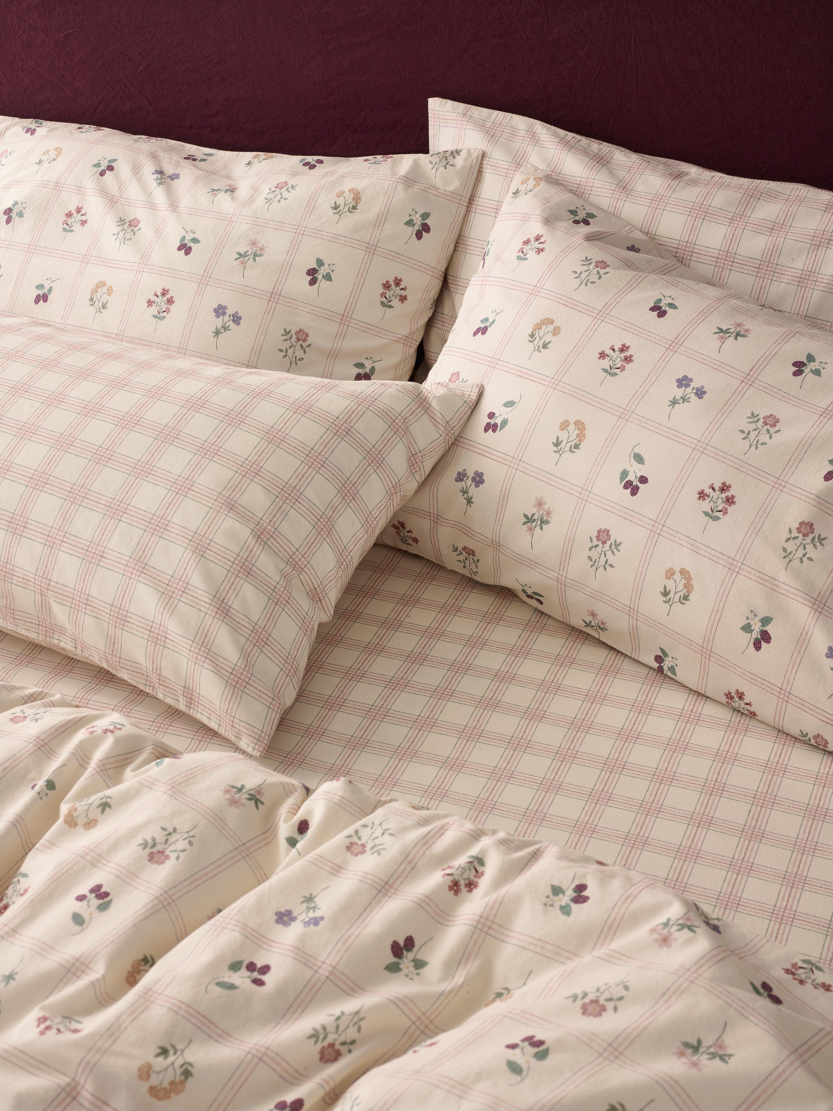 A close-up of a bed dressed in a cream-colored bedding set with a pink plaid pattern and small scattered floral prints, including matching pillowcases.