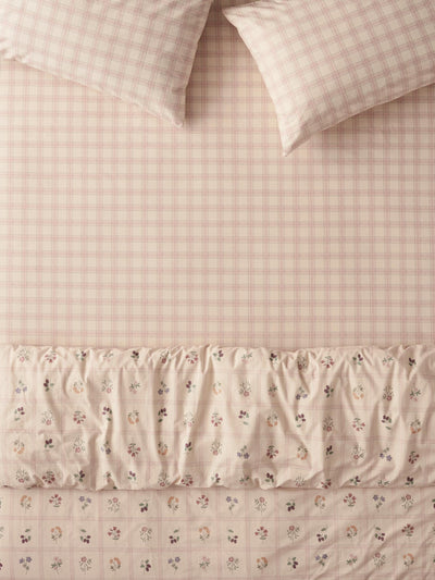 A bedding set featuring a light pink and beige gingham sheet, matching pillowcases, and a ruffled duvet cover with a small floral print.