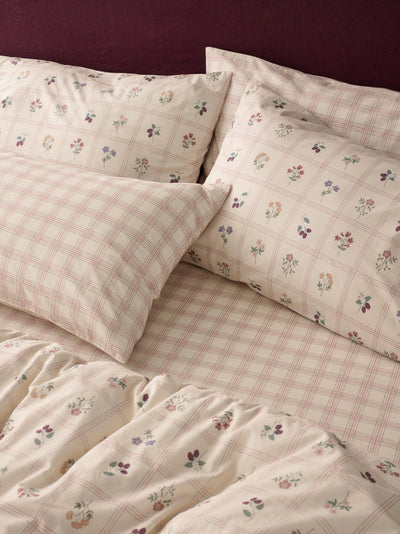 A close-up of a bed dressed in a cream-colored bedding set with a pink plaid pattern and small scattered floral prints, including matching pillowcases.