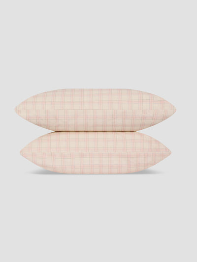 Two pillows stacked vertically, featuring a light pink and white windowpane plaid pattern, set against a solid light gray background.