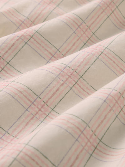 A close-up of draped fabric with a soft plaid pattern in blush pink, muted green, and light blue over a warm off-white base.
