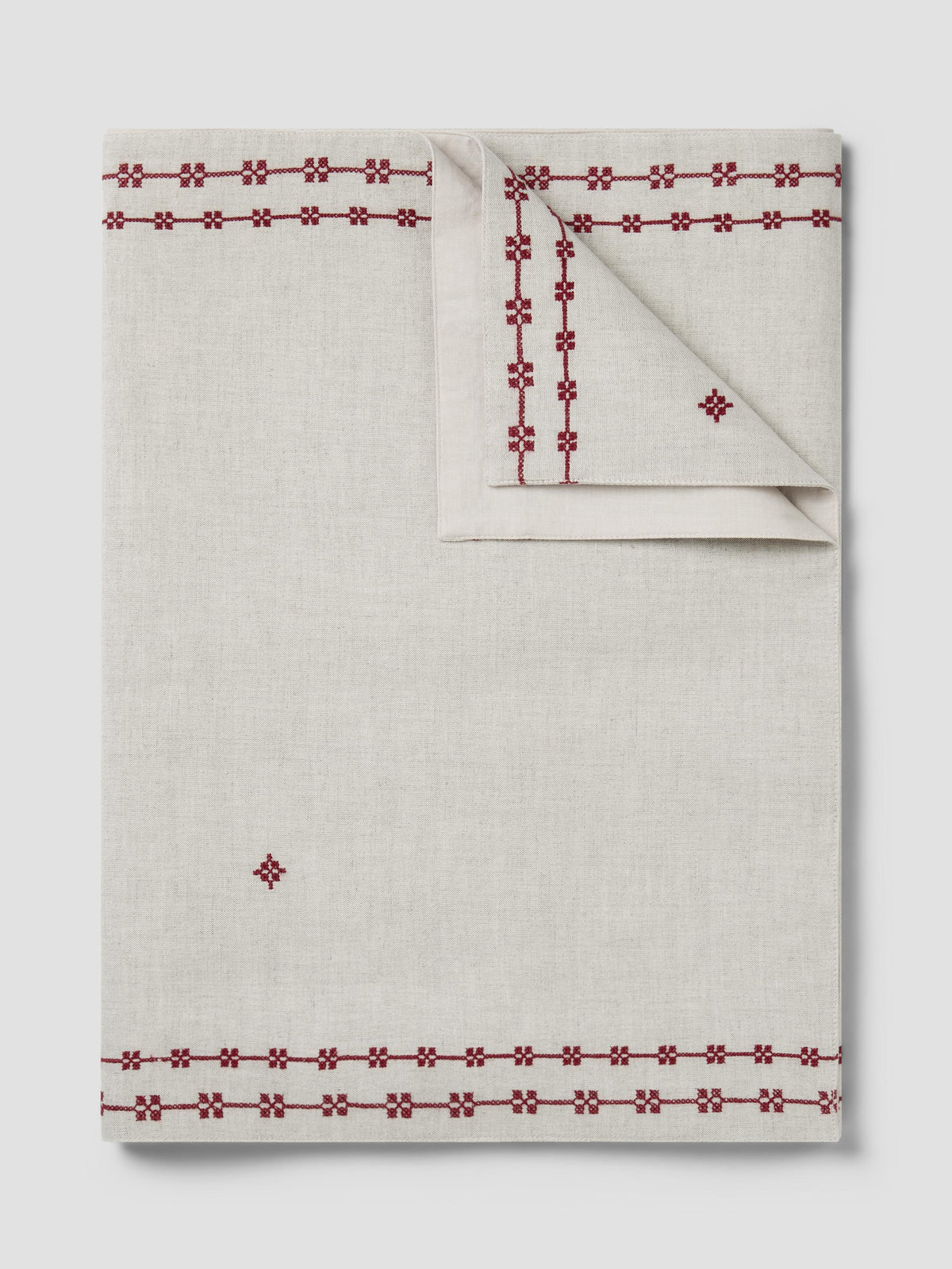 An off-white linen tablecloth with red embroidered geometric borders and a matching folded napkin, displayed on a light gray background.