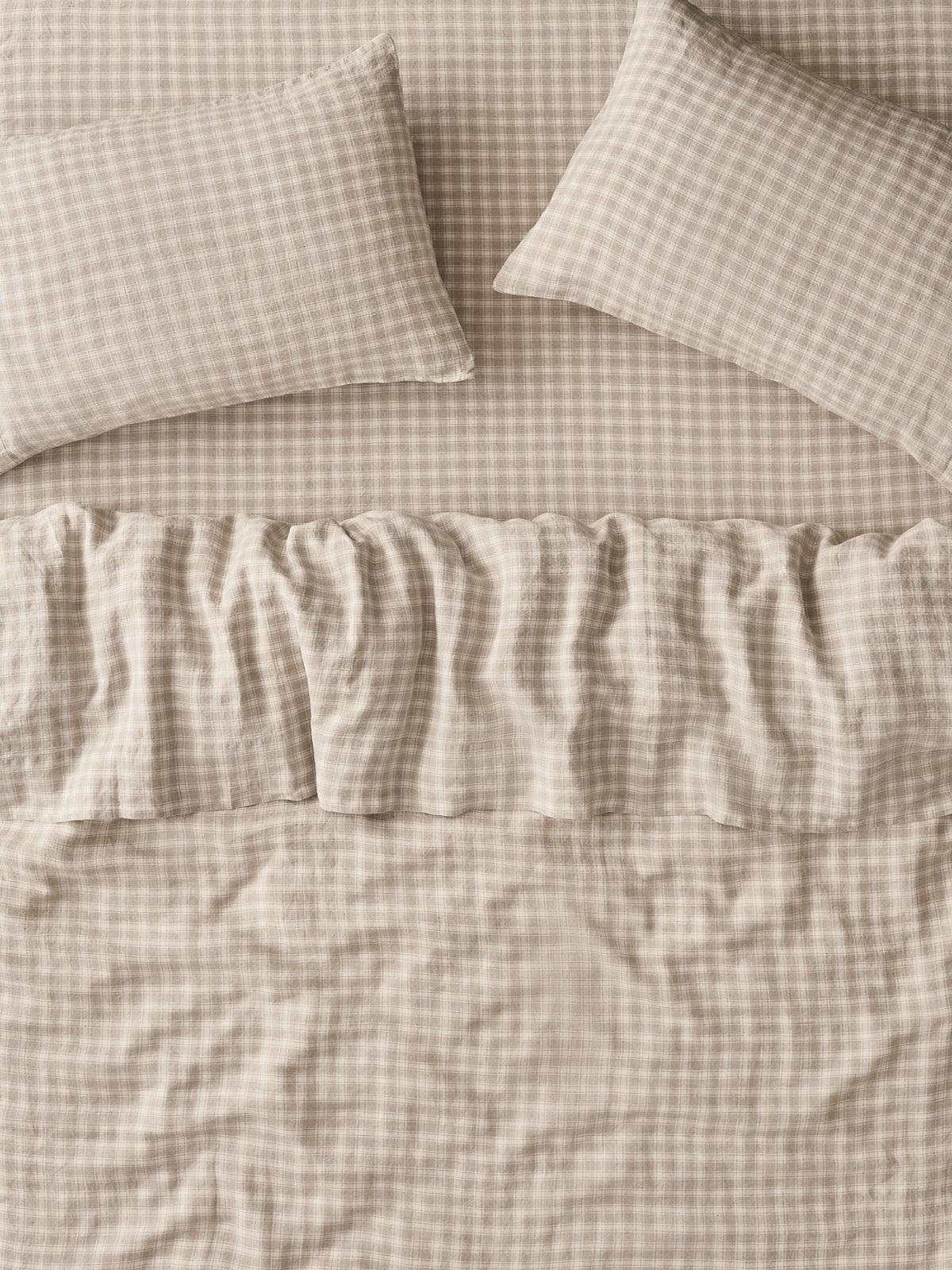 A close-up of a beige and white gingham bedding set, featuring a ruffled bedspread and two matching pillowcases.