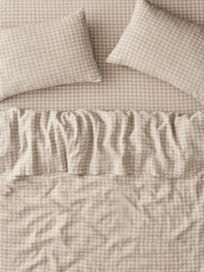 A close-up of a beige and white gingham bedding set, featuring a ruffled bedspread and two matching pillowcases.