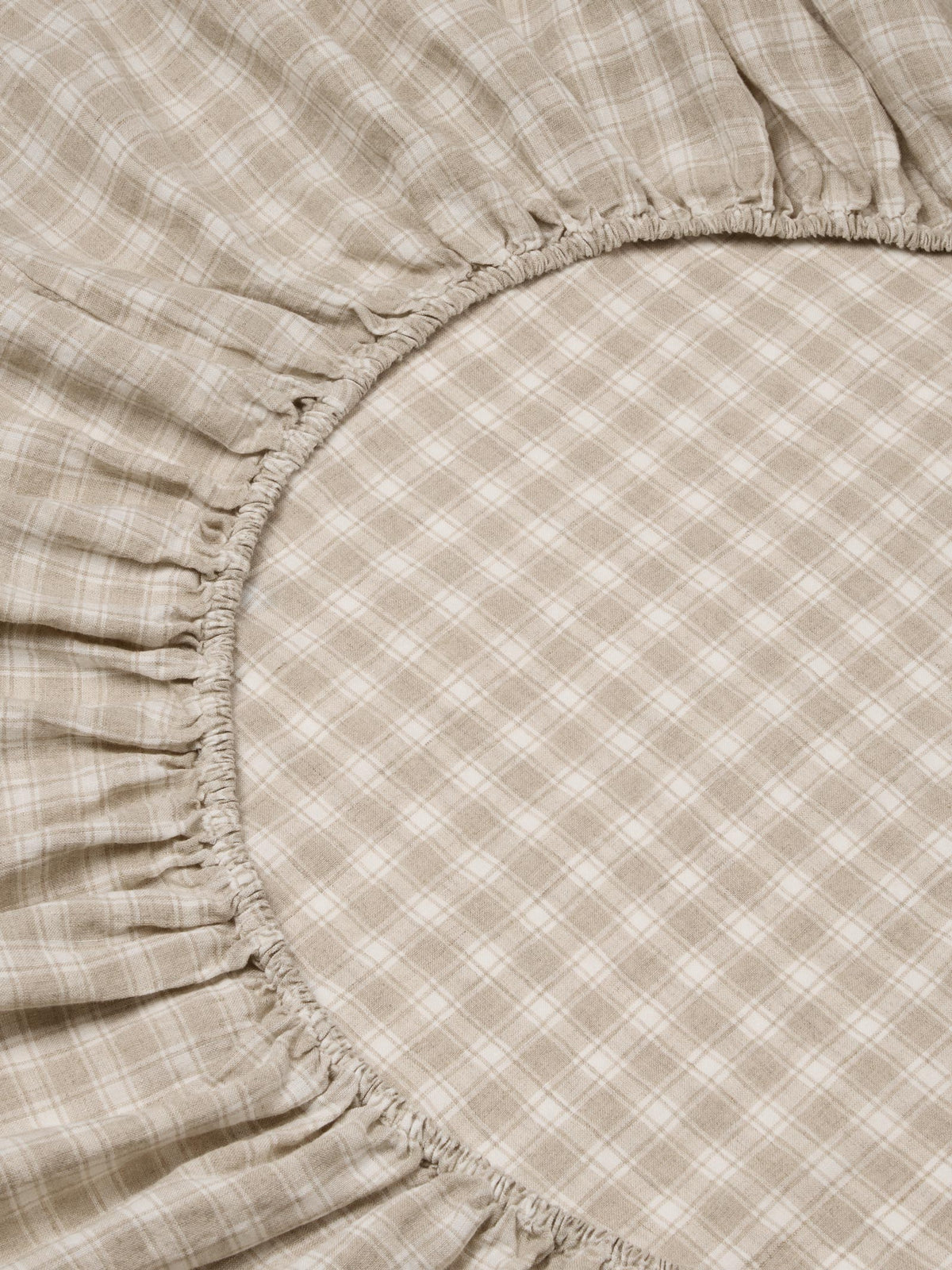Close-up of a beige and white plaid sheet with gathered ruffled edges, filling the frame.