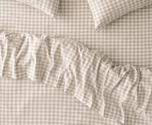 A close-up of a beige and white gingham bedding set with a ruffled duvet cover and two matching pillowcases.