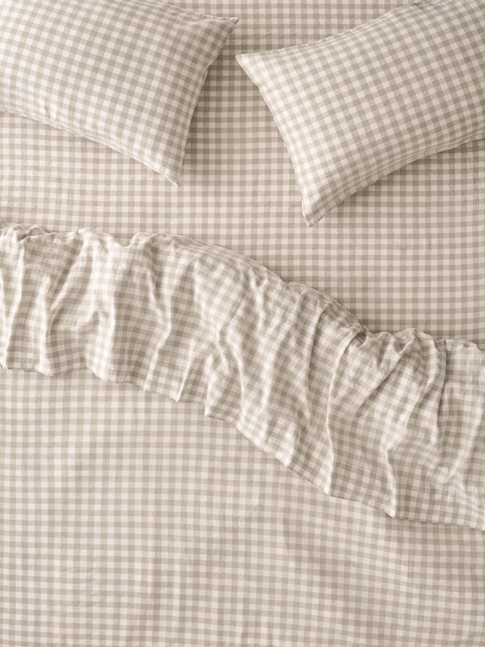 A close-up of a beige and white gingham bedding set with a ruffled duvet cover and two matching pillowcases.