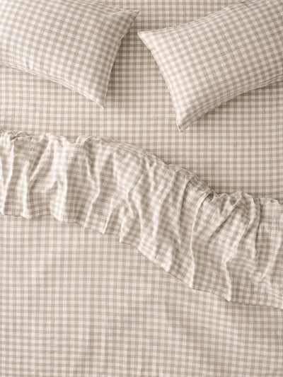 A close-up of a beige and white gingham bedding set with a ruffled duvet cover and two matching pillowcases.