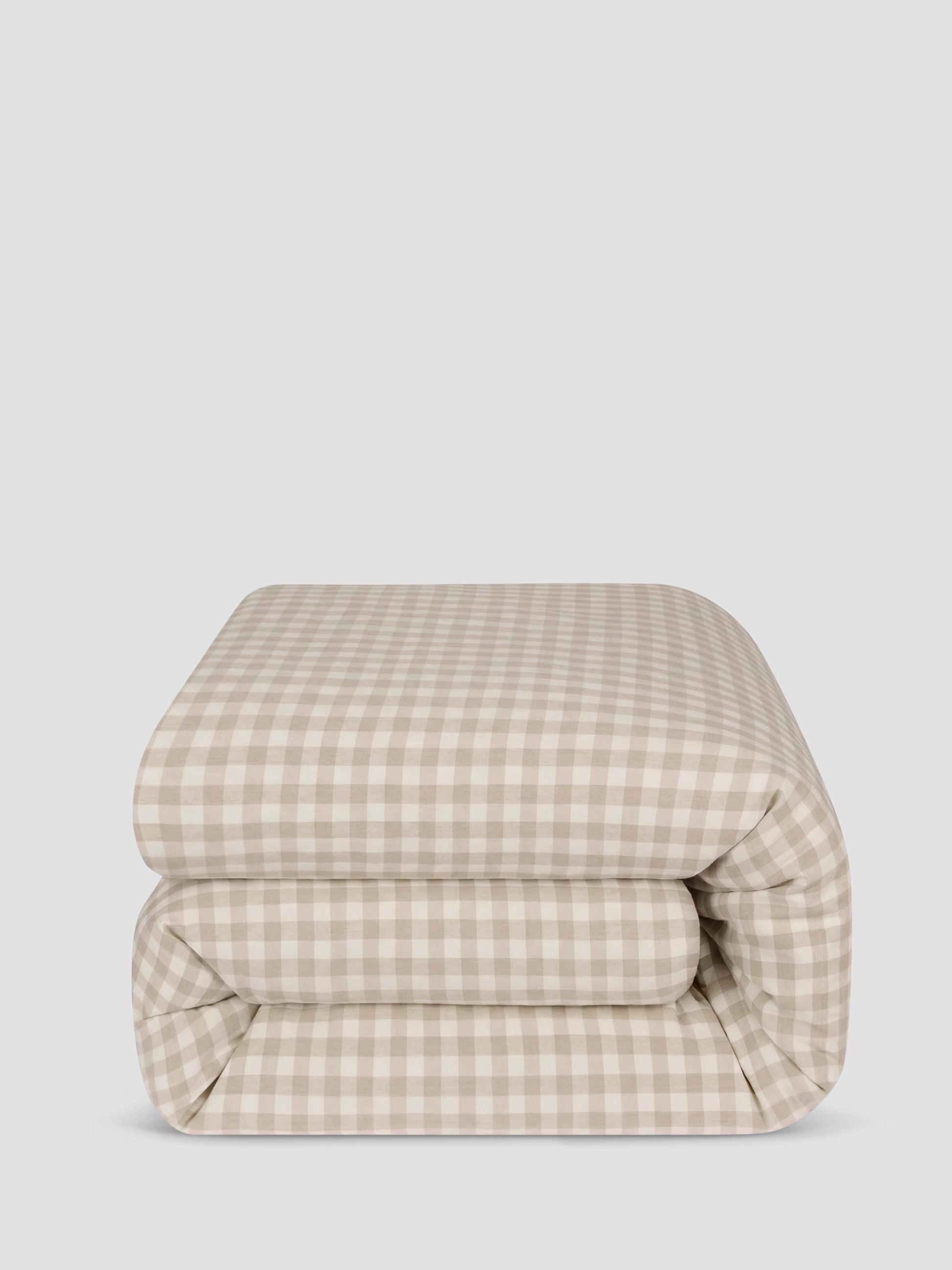 A folded comforter, featuring a beige and off-white gingham check pattern, set against a solid light gray background.