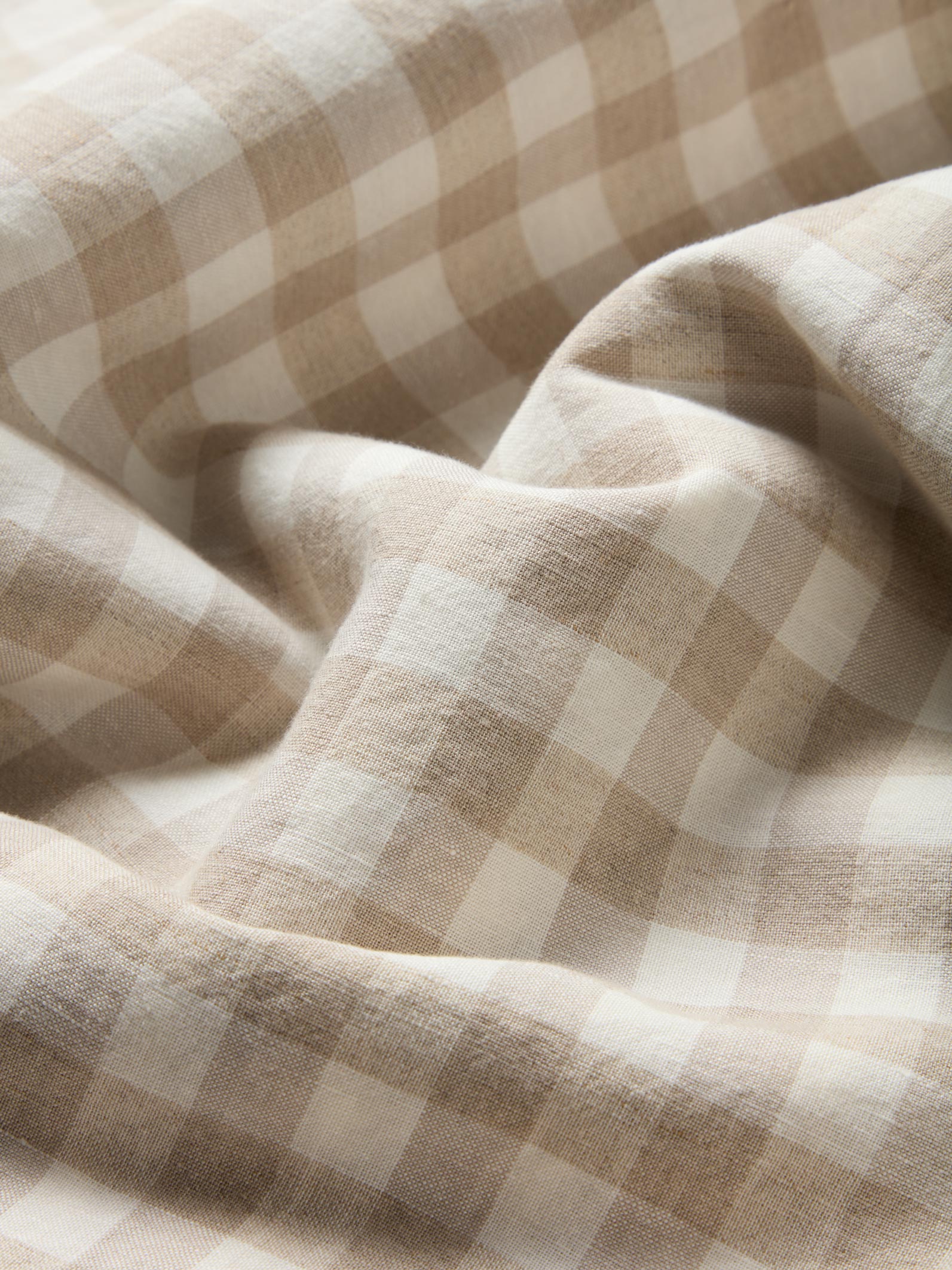 A close-up of draped fabric with a soft beige and off-white gingham check pattern.