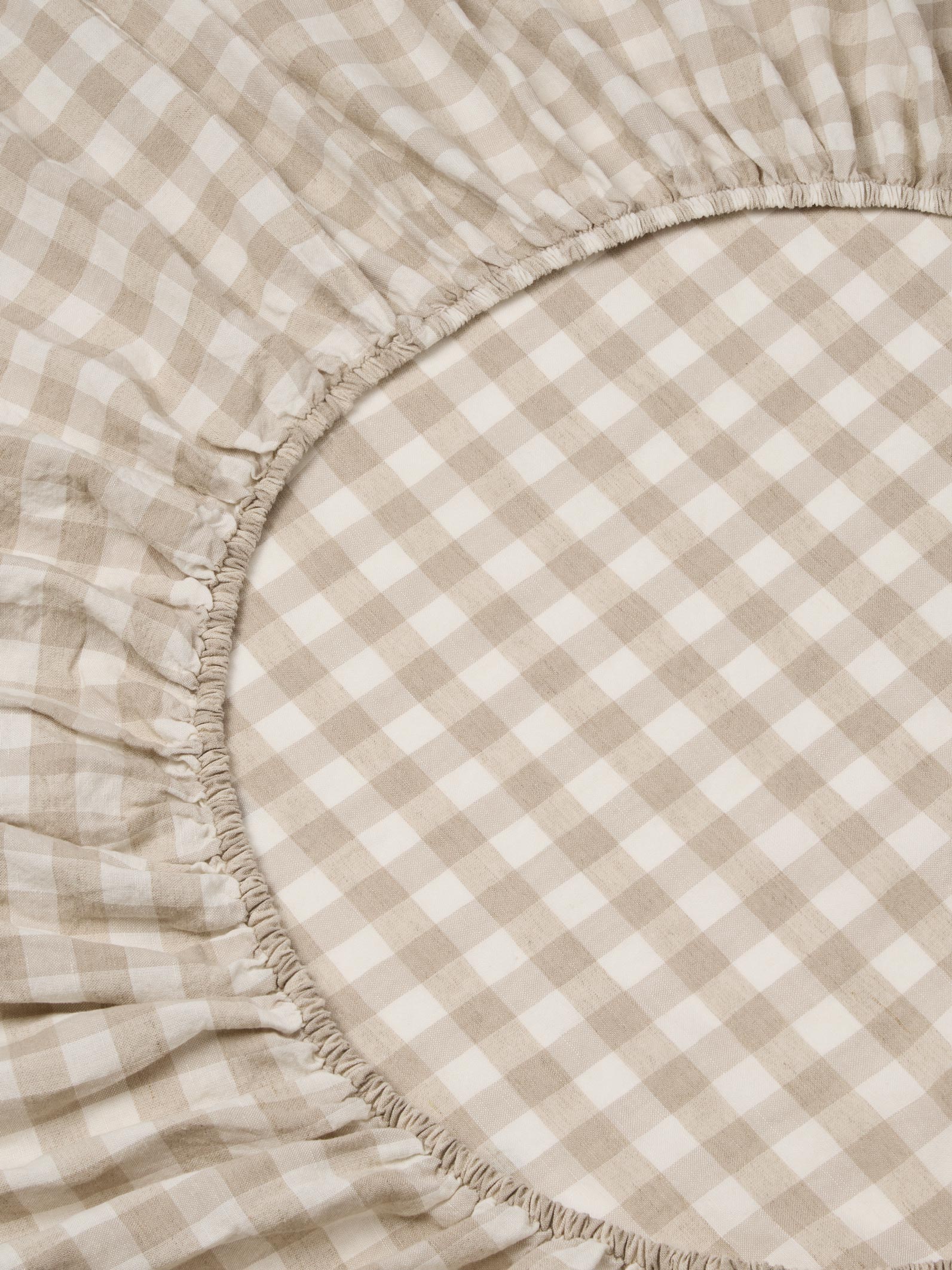 Close-up of a beige and off-white gingham check fitted sheet with a gathered elasticized edge.