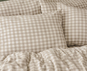 Beige and white gingham check bedding set with matching pillowcases and a ruffled duvet cover, styled on a bed against a textured green headboard.