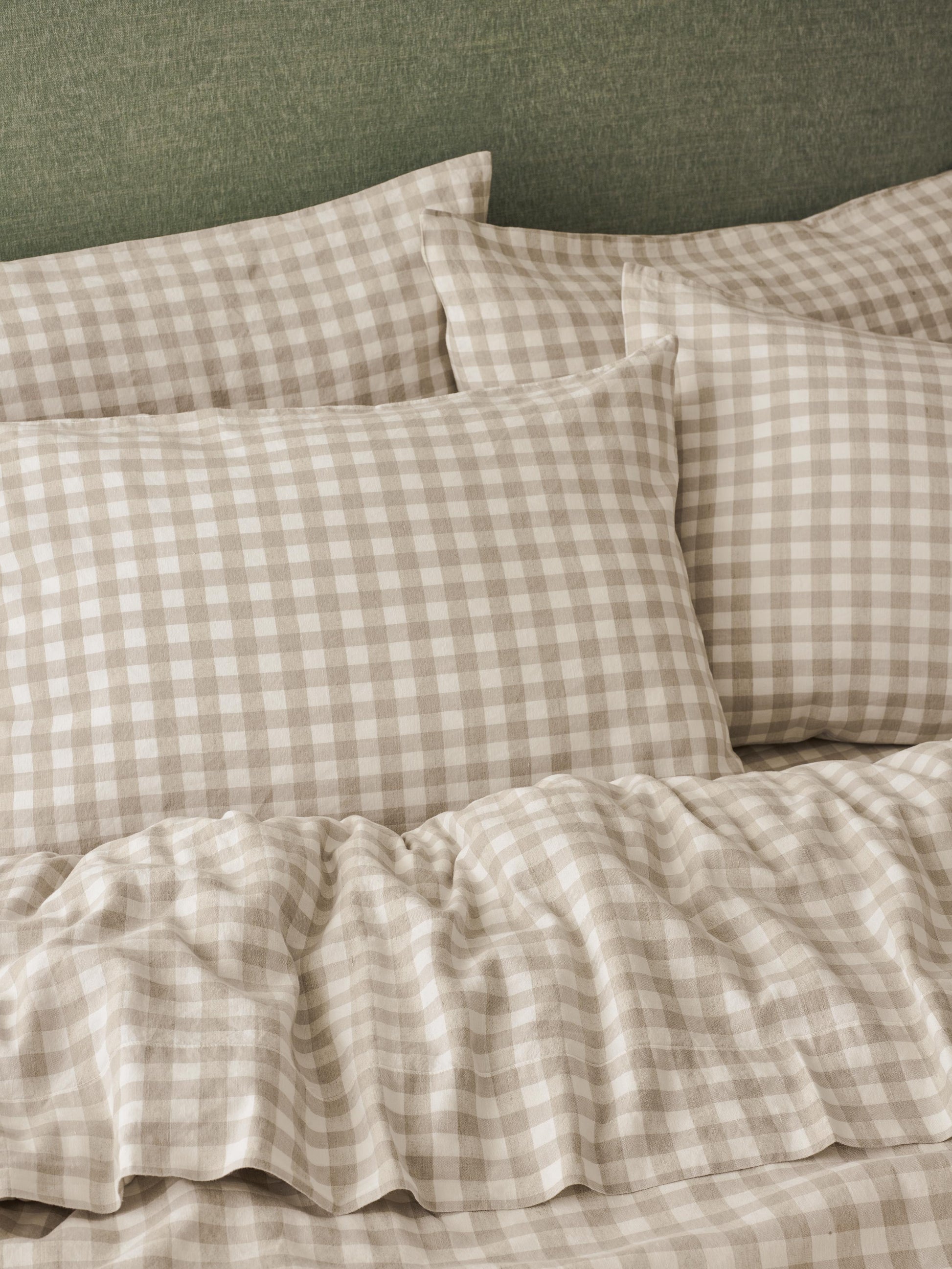 Beige and white gingham check bedding set with matching pillowcases and a ruffled duvet cover, styled on a bed against a textured green headboard.